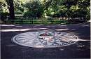 [button photo of flowers on John Lennon’s memorial “Imagine” in Central Park, NY city.]